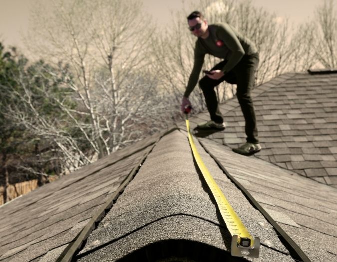 Man on top of a roof getting measurements with tape measure.