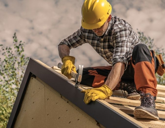 Man on top of a roof, wearing a hard hat with a hammer, replacing roof.