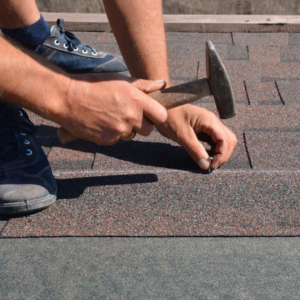 Close up shot of a nail being hammered down between shingles