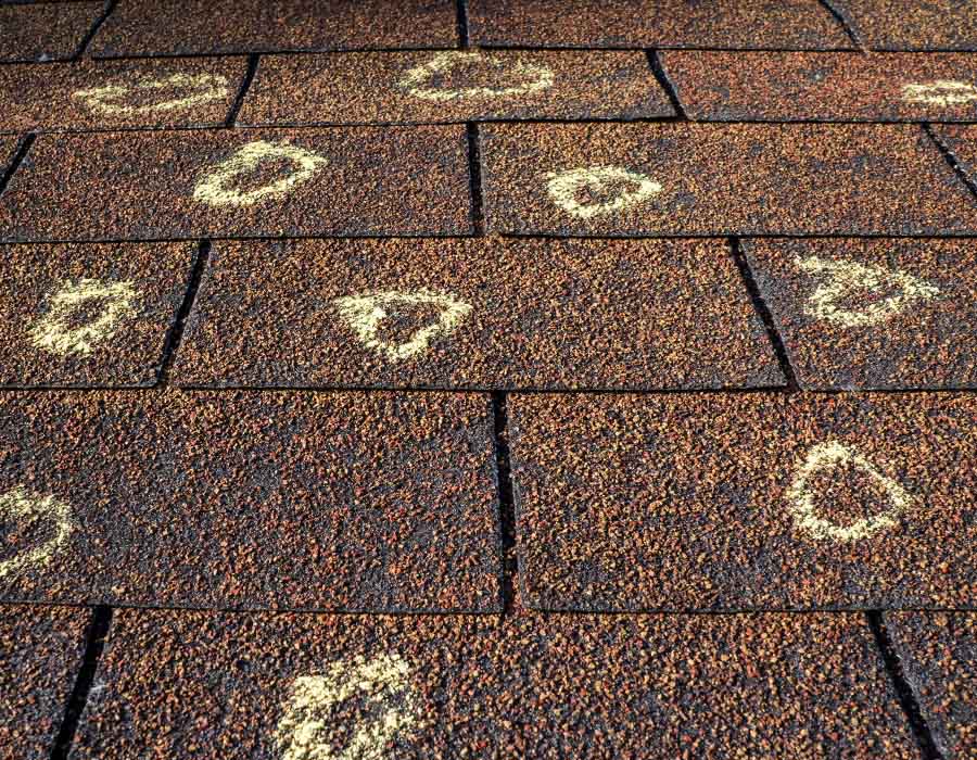 Close up shot of roof shingles with chalk marks, indicating potential roof damage