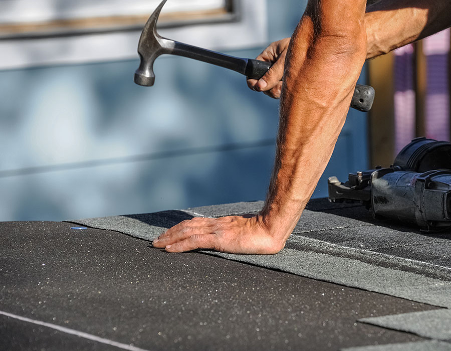 Close up shot of a man's hands, holding a hammer on top of a roof